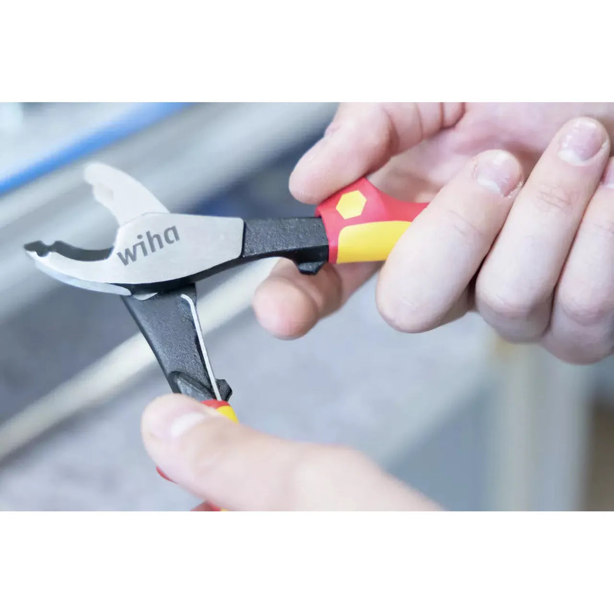 Person holding a red and yellow-handled cable cutter with black and silver blades.