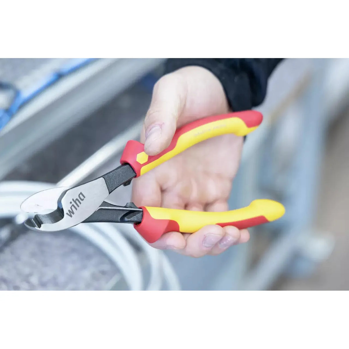 A person holding red and yellow insulated cable cutters, with metallic jaws, near cables.