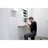 A person kneels while using an electric screwdriver on an open electrical panel