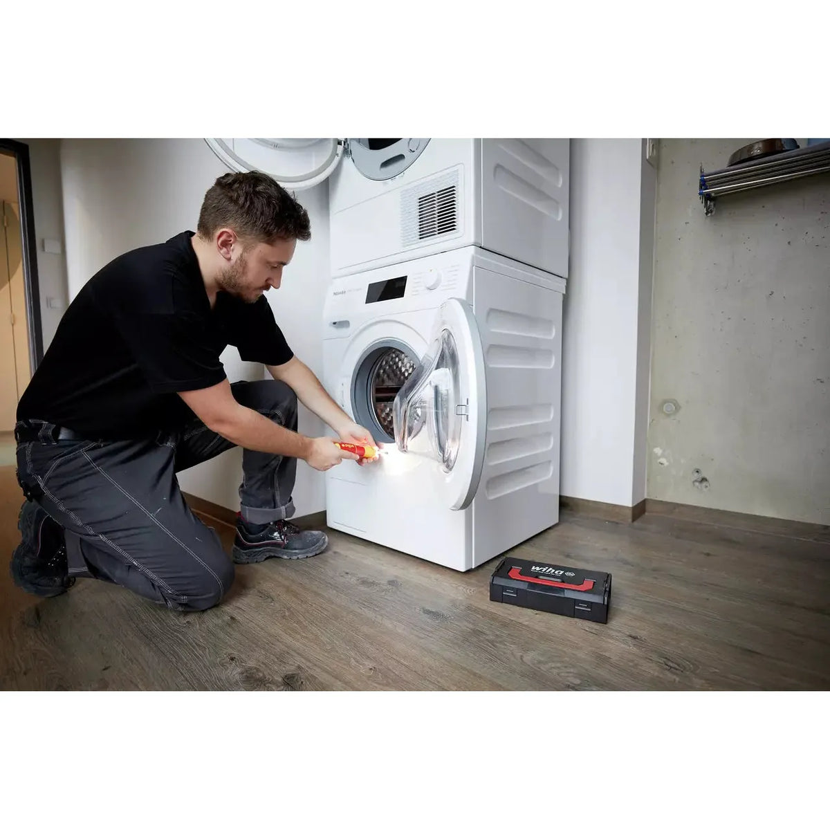 A person using an electric screwdriver to work on a washing machine door.
