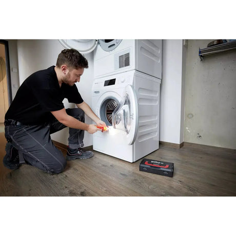 A person using an electric screwdriver to work on a washing machine door.