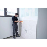 A person using an electric screwdriver on a tiled wall in a bright room.