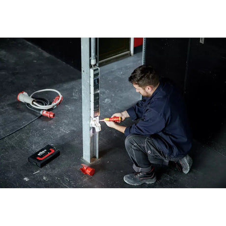 A man works with an electric screwdriver on an outlet on a metal post.