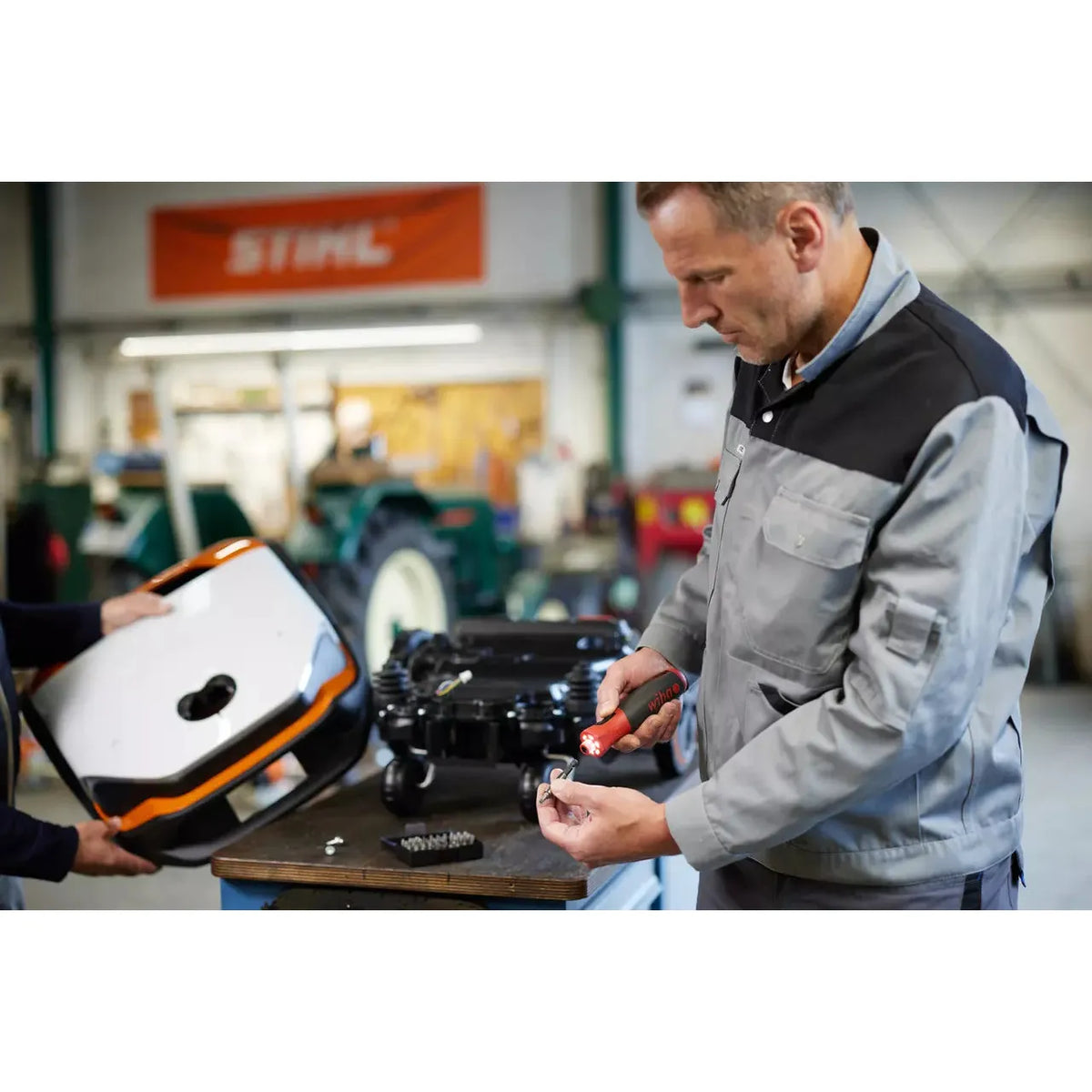 Two people working in a workshop with an electric screwdriver and a device cover.