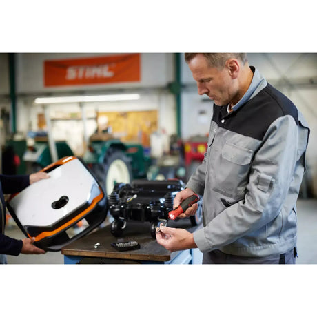 Two people working in a workshop with an electric screwdriver and a device cover.