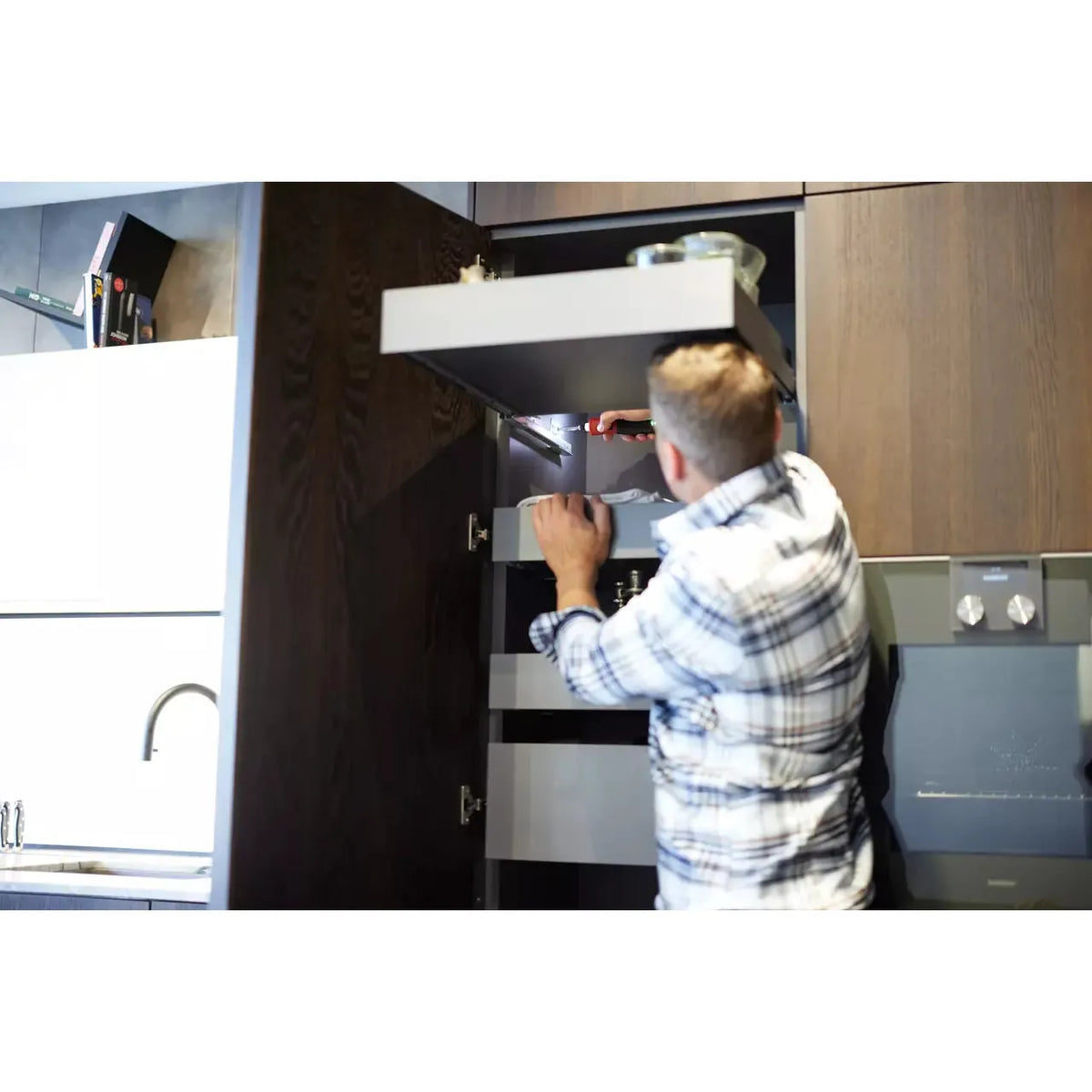 A person uses a screwdriver inside a kitchen cabinet.