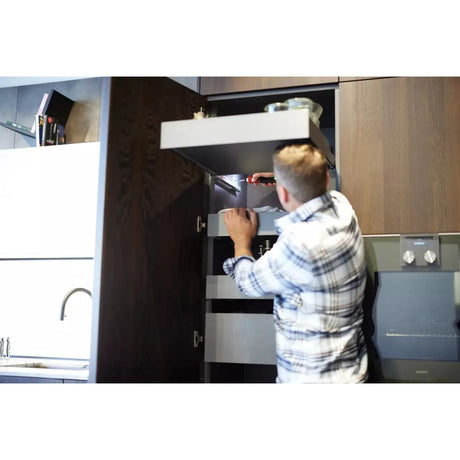 A person uses a screwdriver inside a kitchen cabinet.