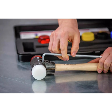 A person adjusts a mallet with a hex key on a metal surface.