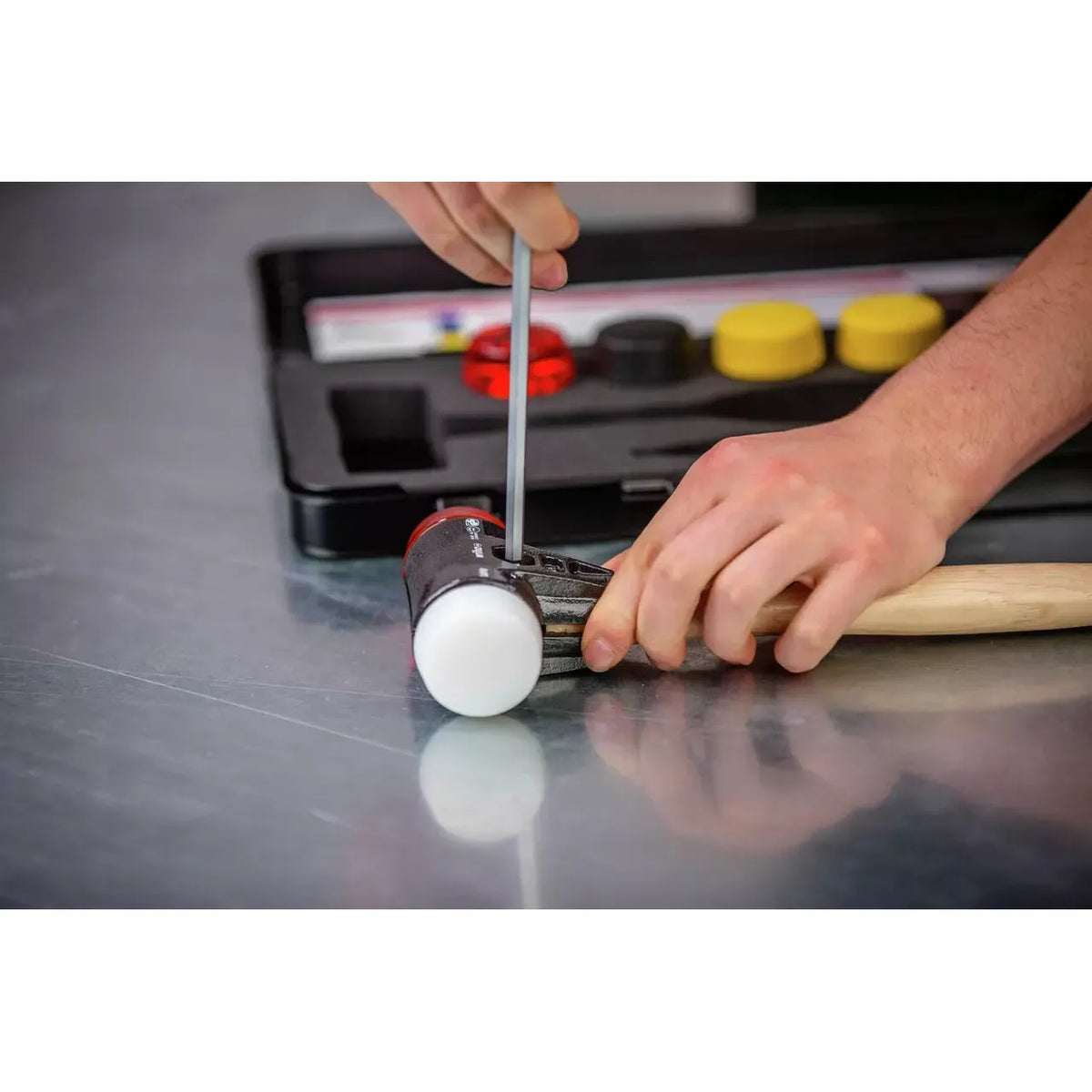 A person assembling a mallet with white rubber heads using a tool, with a tool case in the background.
