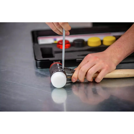 A person assembling a mallet with white rubber heads using a tool, with a tool case in the background.