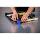 Person assembling a mallet with blue head and wooden handle on a metal surface