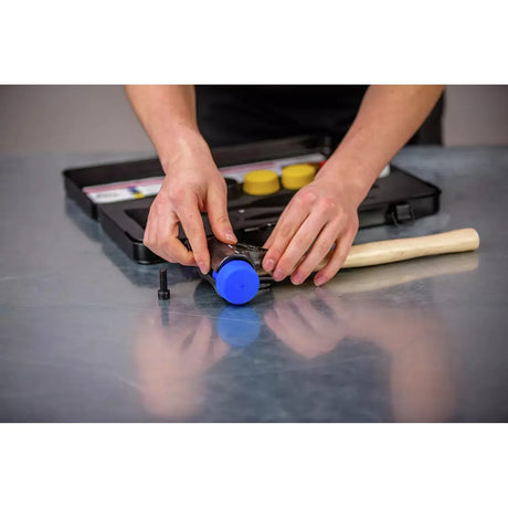 Person assembling a mallet with blue head and wooden handle on a metal surface