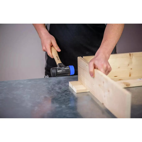 A person using a mallet with a blue rubber head to assemble wooden boards.