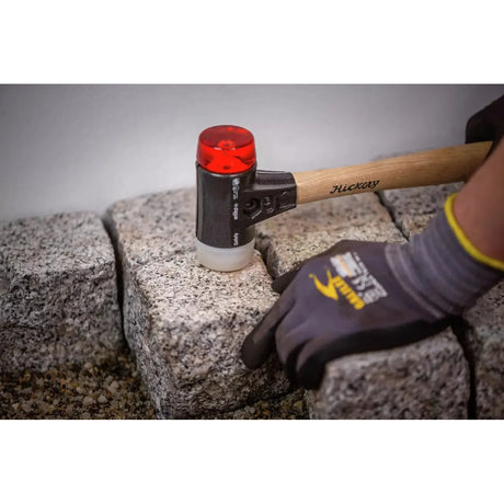 A person using a mallet with a wooden handle and rubber head to adjust stone pavers.