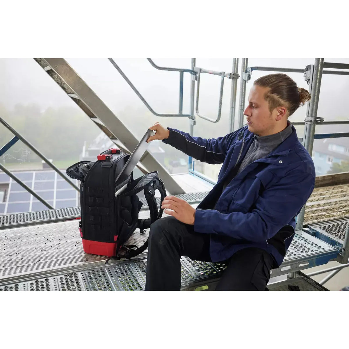 Person on scaffolding placing a laptop into a black backpack.
