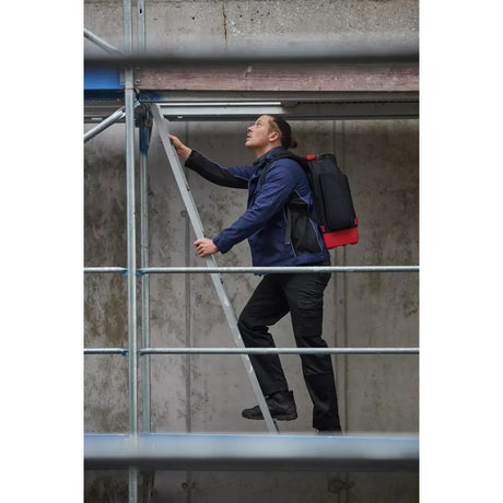 A person climbs a metal ladder on a scaffold, wearing a blue jacket and black pants.
