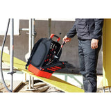 Person taking a screwdriver from a black and red tool backpack on a construction site.