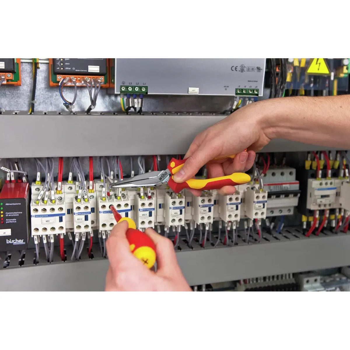 Two hands using pliers and screwdriver on electrical components in a panel.