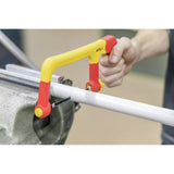 A person using a yellow and red hacksaw to cut a white pipe held in a vise.