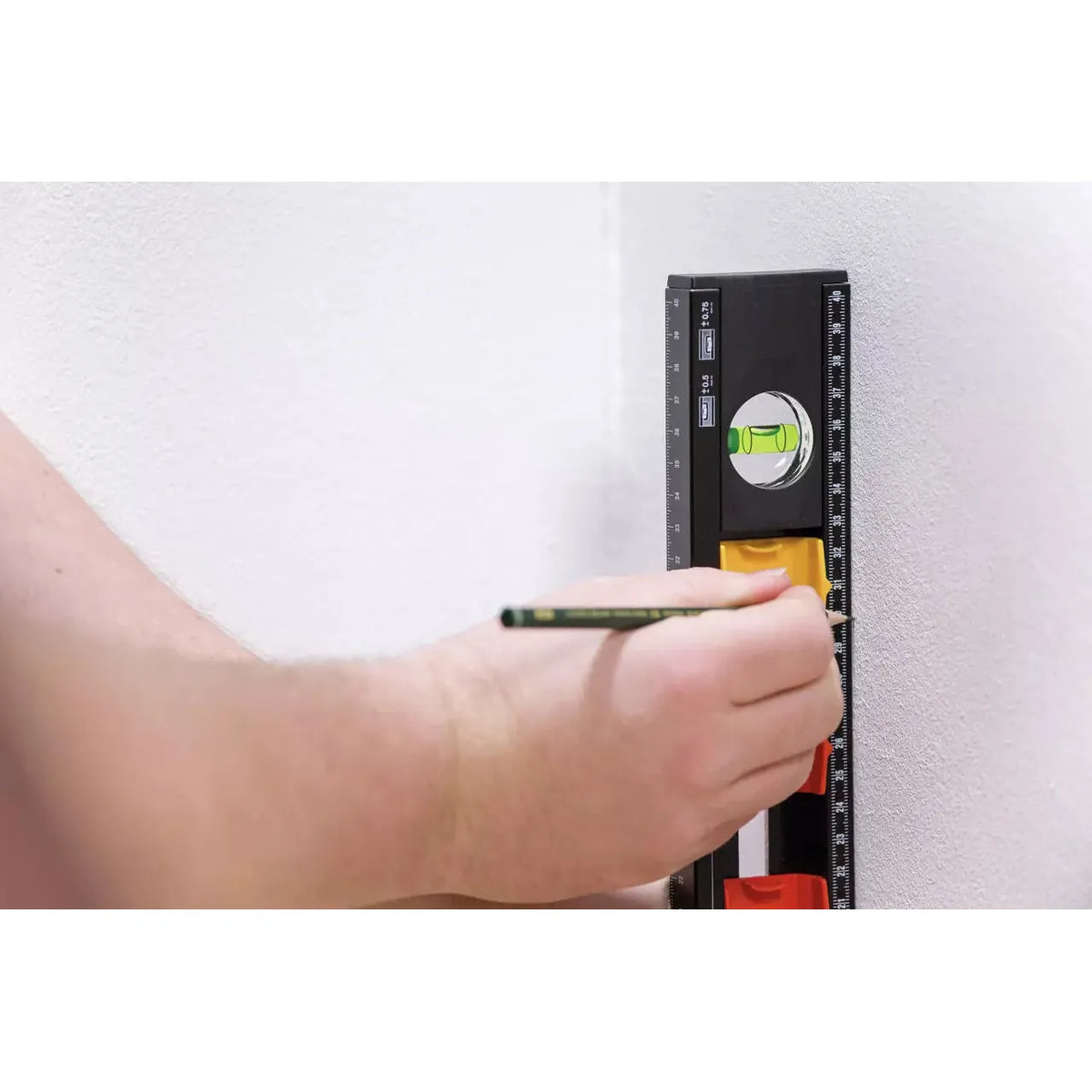 A person using a black and yellow level on a white wall, marking with a pencil.