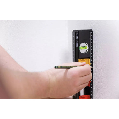 A person using a black and yellow level on a white wall, marking with a pencil.