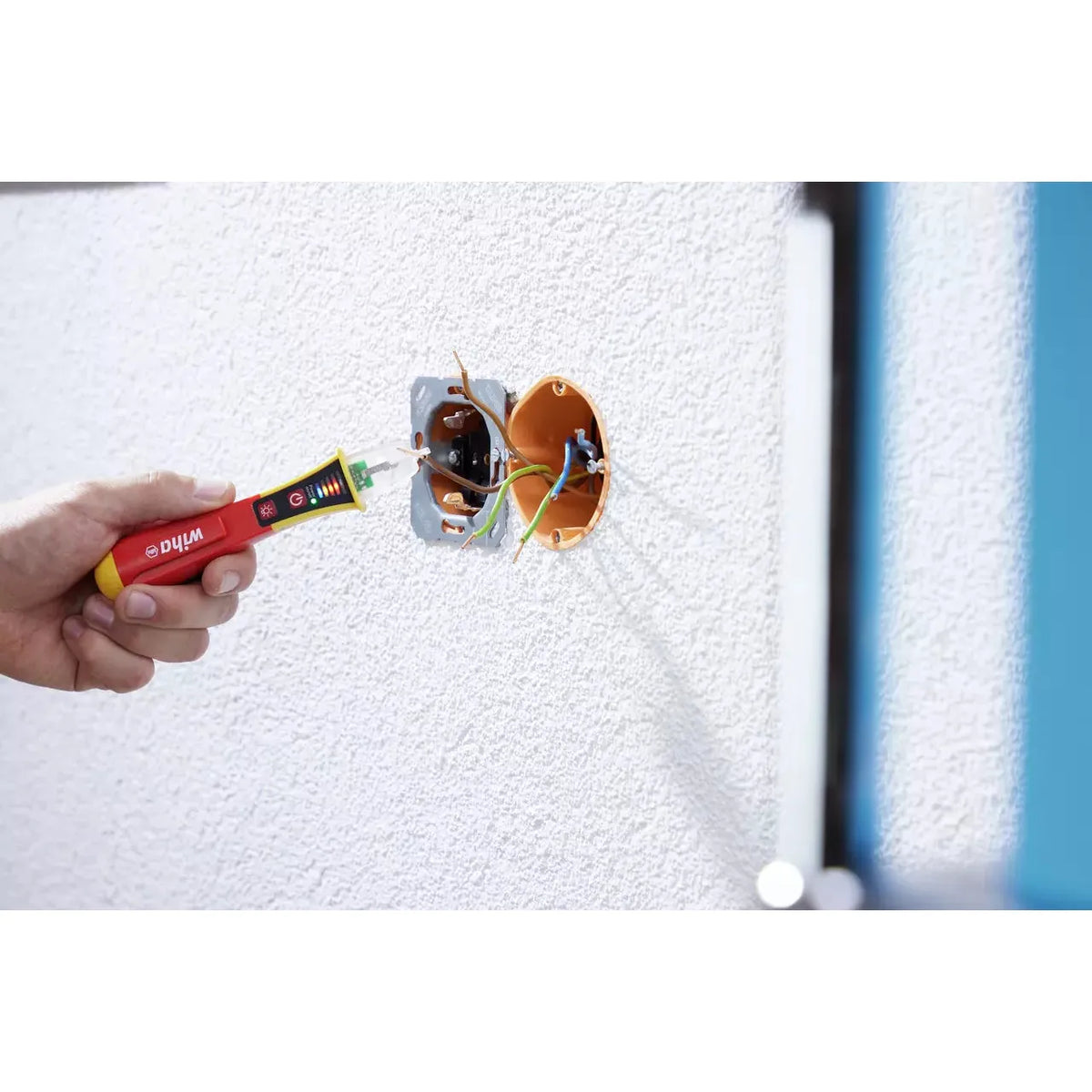 12–1,000V AC – Hand using a non-contact voltage detector near exposed wires in a wall socket