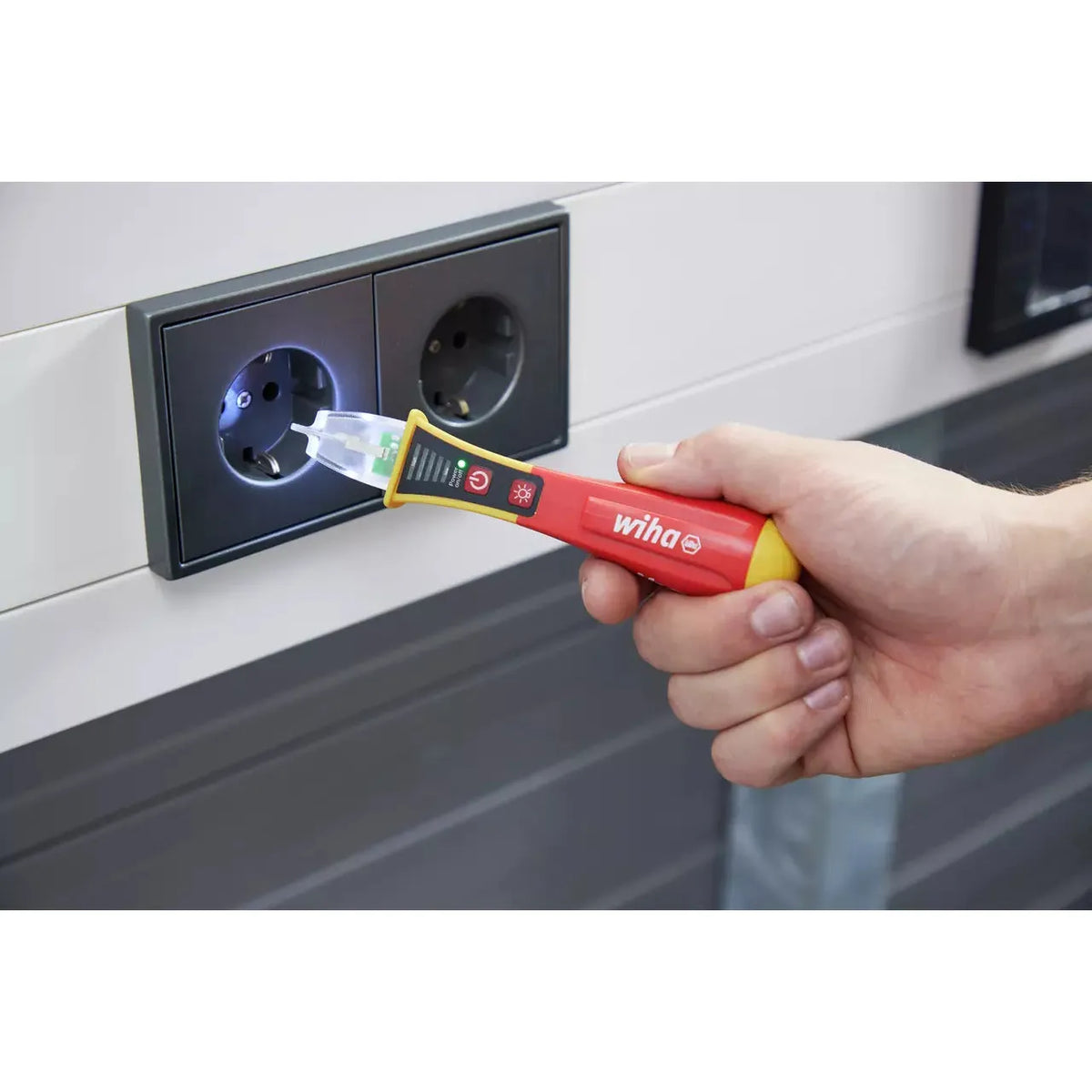 12–1,000V AC – Hand holding a non-contact voltage detector near a power socket.