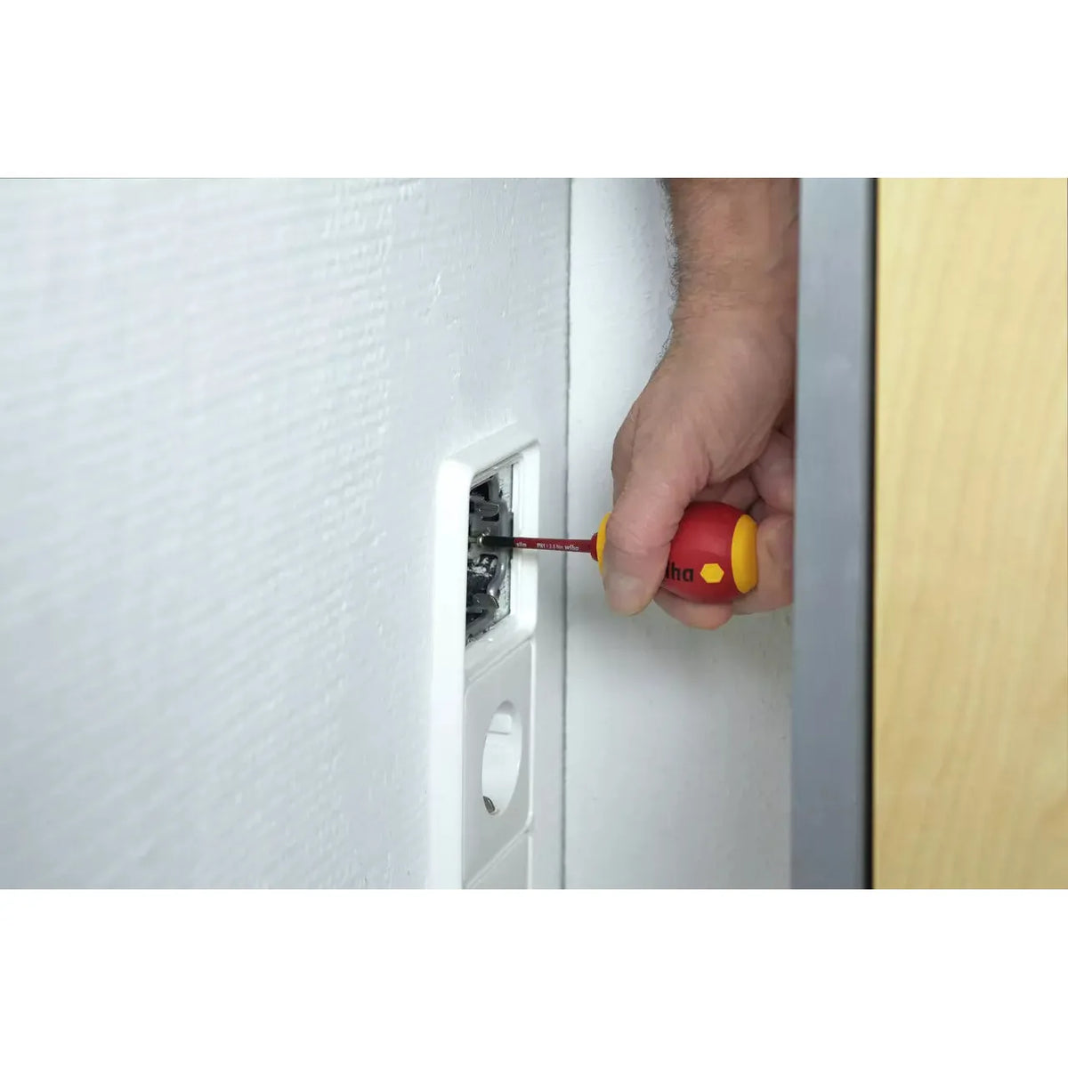 A person using a red and yellow screwdriver to work on a wall socket