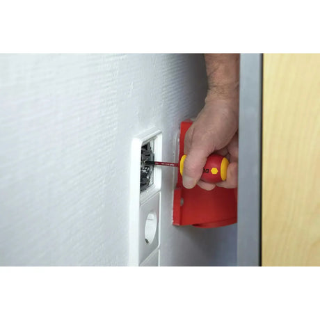 Person using a red and yellow stubby screwdriver on a wall socket