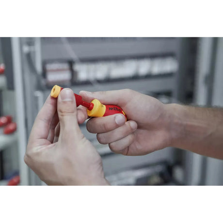Person holding a red and yellow electric screwdriver with adapter in an industrial setting.