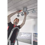 A person on a ladder installs a ceiling light using a screwdriver.