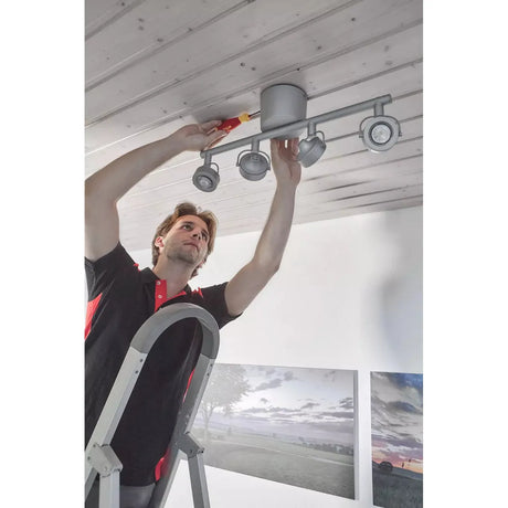 A person on a ladder installs a ceiling light using a screwdriver.