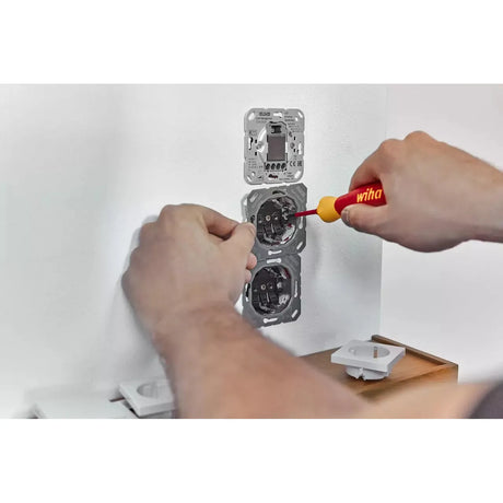 Person using a red and yellow screwdriver to install sockets in a wall