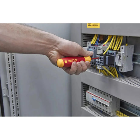 Hand using an electric screwdriver on an electrical panel with yellow wires.