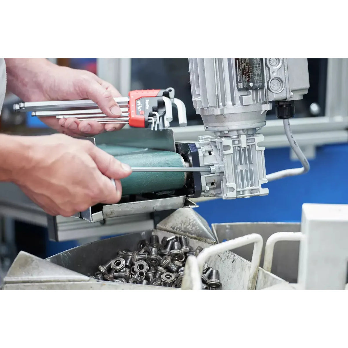 Person using a hex key set on a machine with bolts in the foreground.