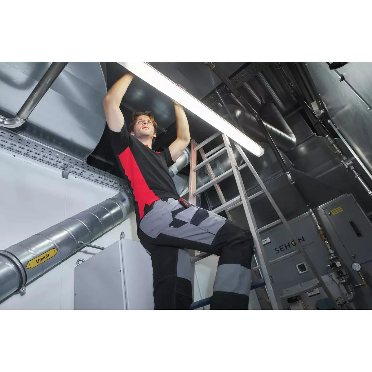Person working on a ceiling light in a technical room with ventilation ducts.