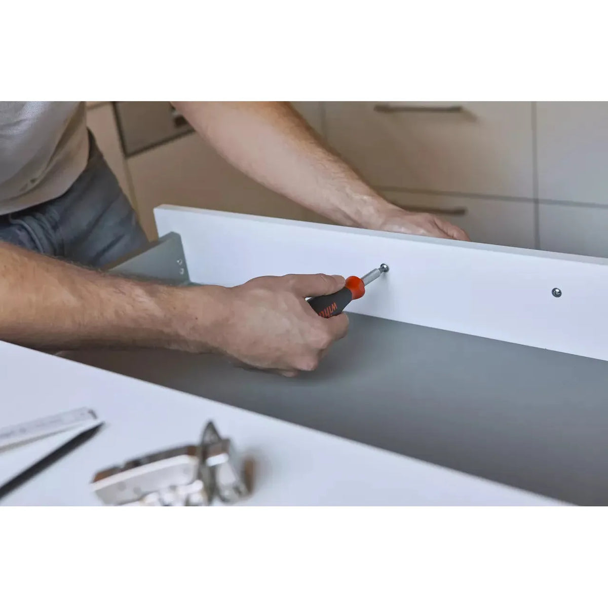 Person using screwdriver on white drawer in kitchen