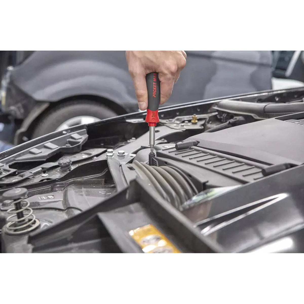 A person uses a screwdriver in a car engine compartment.