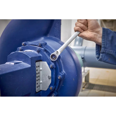 A person uses a ratchet wrench on a large blue industrial machine.