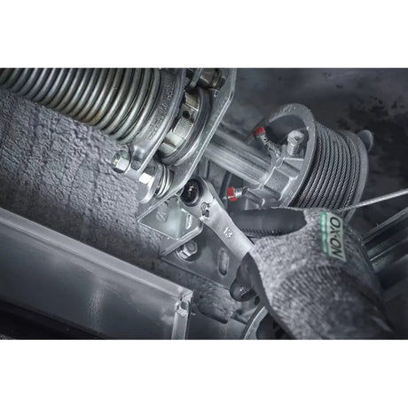 A hand in a glove uses a ratchet wrench on a metal garage door mechanism.