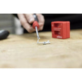 A hand holding a screwdriver with screws attracted to its tip on a wooden surface.