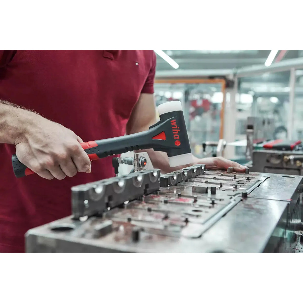 Person using black hammer with white plastic head in workshop