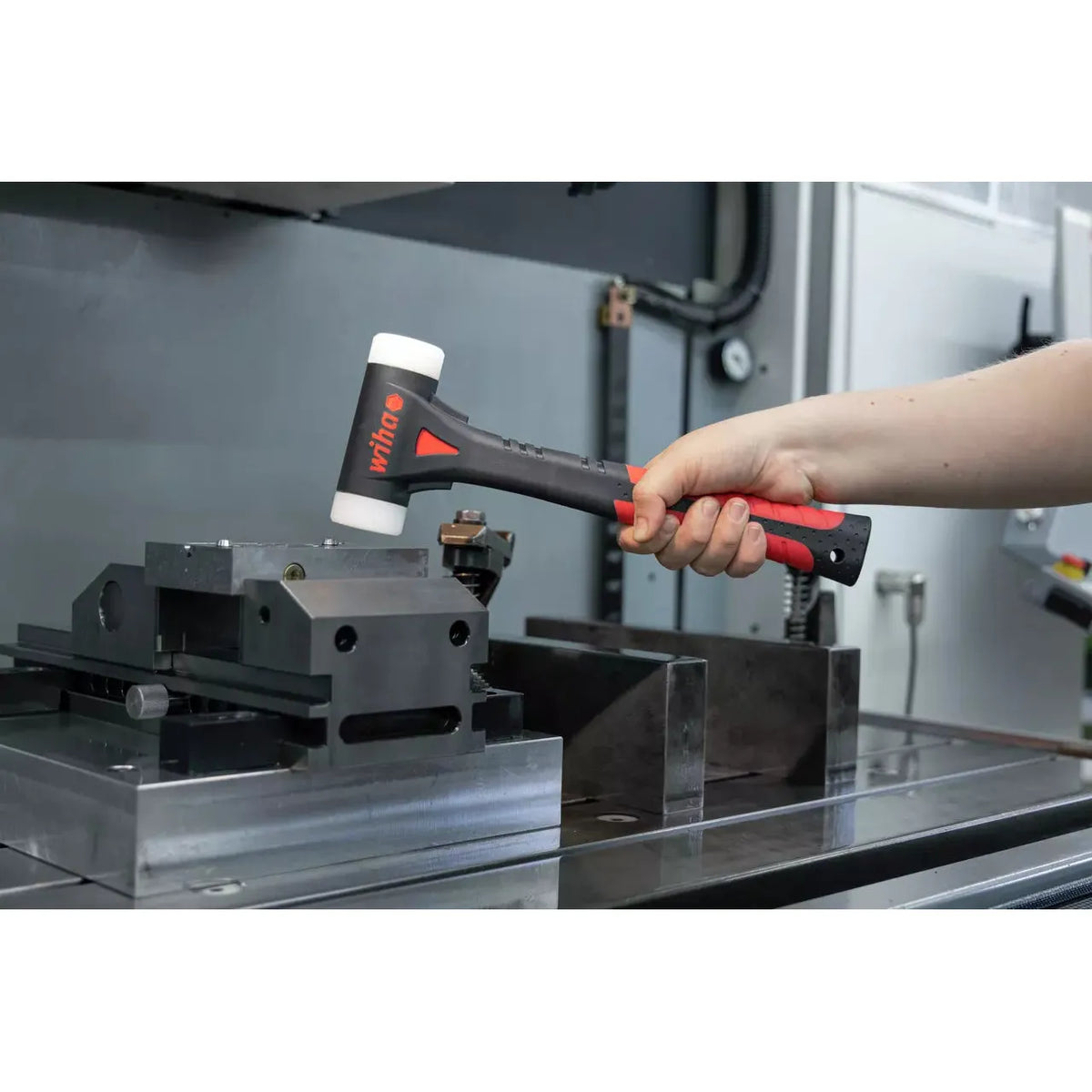 A person holding a black and red dead-blow hammer with white ends near a metal vice.