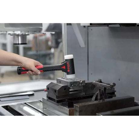 A person uses a dead-blow hammer on a metal workpiece in a workshop.