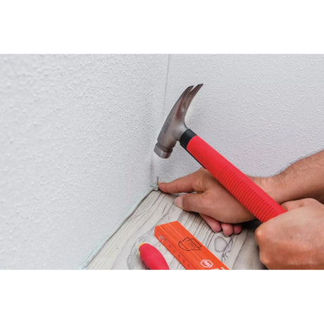 Person using a red-handled hammer to secure a cable clip on a baseboard.