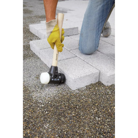 Person using a mallet with a wooden handle to lay paving stones on gravel.