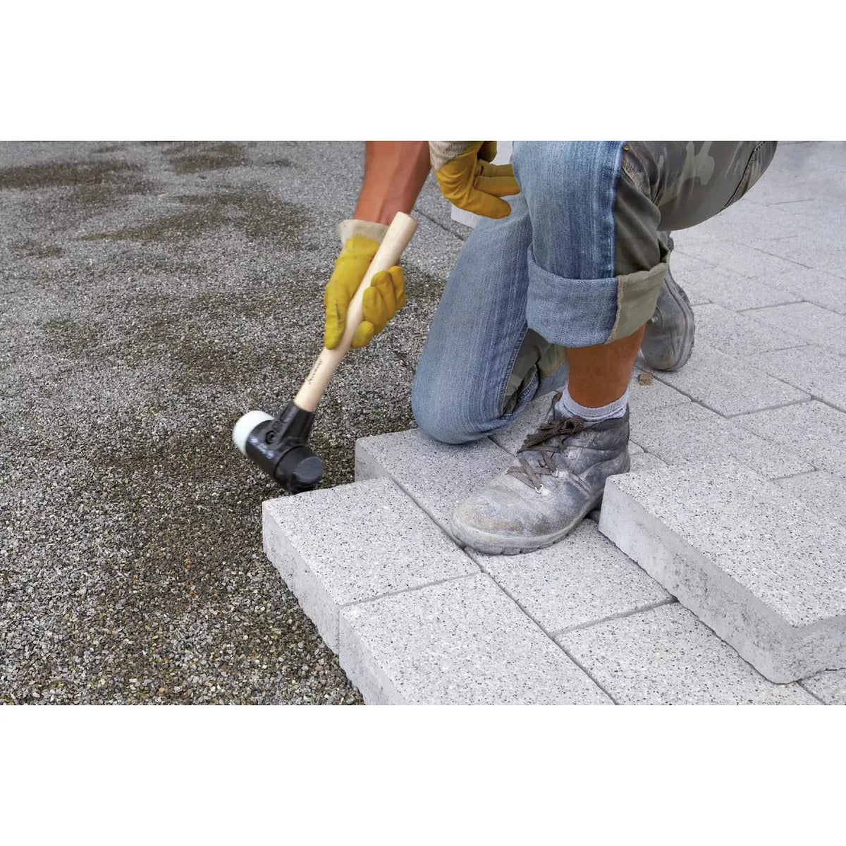 Person using a rubber mallet to lay paving stones
