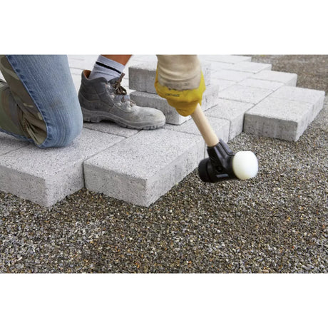 Person using a rubber mallet to lay paving stones on gravel