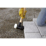 A person using a rubber mallet to adjust paving stones on gravel ground.