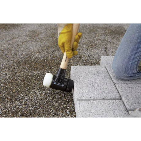 A person using a rubber mallet to adjust paving stones on gravel ground.
